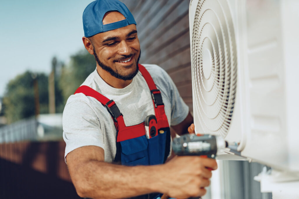 repairman in uniform installing the outside unit of air conditioner